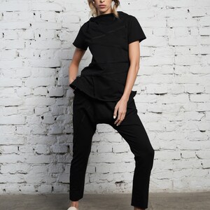 May include: A black mock neck shirt with a layered design and black pants. The shirt has multiple zippers along the seams. The person is wearing white sandals.