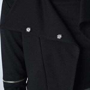 Puede incluir: Chaqueta negra corta con detalle de cremallera y botones plateados. La chaqueta tiene un cuello que se puede llevar subido o bajado.