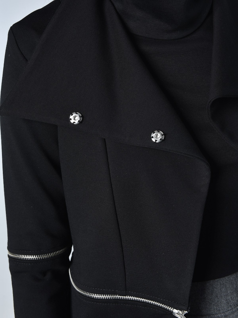 Puede incluir: Chaqueta negra corta con detalle de cremallera y botones plateados. La chaqueta tiene un cuello que se puede llevar subido o bajado.