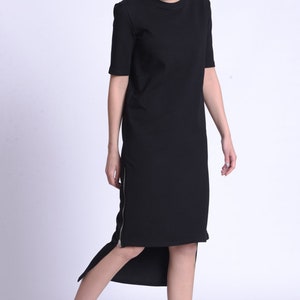 Puede incluir: Un vestido midi negro con cremallera lateral y bajo asim&eacute;trico. El vestido est&aacute; hecho de una tela suave y c&oacute;moda, perfecto para un look casual. La modelo lleva zapatillas negras con suela blanca.