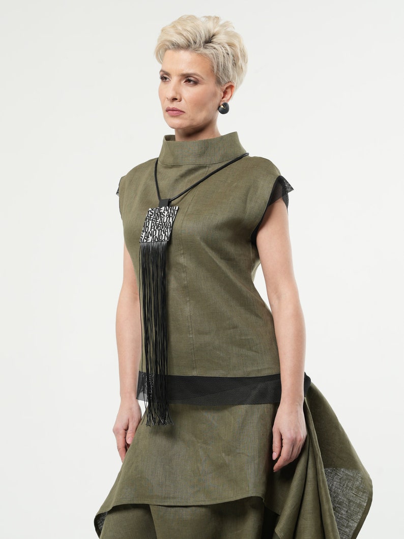 Puede incluir: Conjunto de top y falda de lino verde oliva. El top tiene cuello alto y detalles de malla negra. Un collar negro con colgante cuadrado y flecos. La falda tiene un dise&ntilde;o en capas. Pendientes negros completan el look.