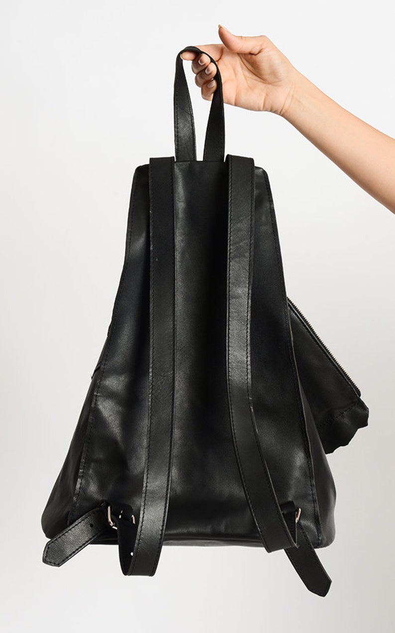 May include: Black leather backpack with adjustable straps and a zippered pocket. The backpack has a triangular shape and is made of a soft, supple leather.