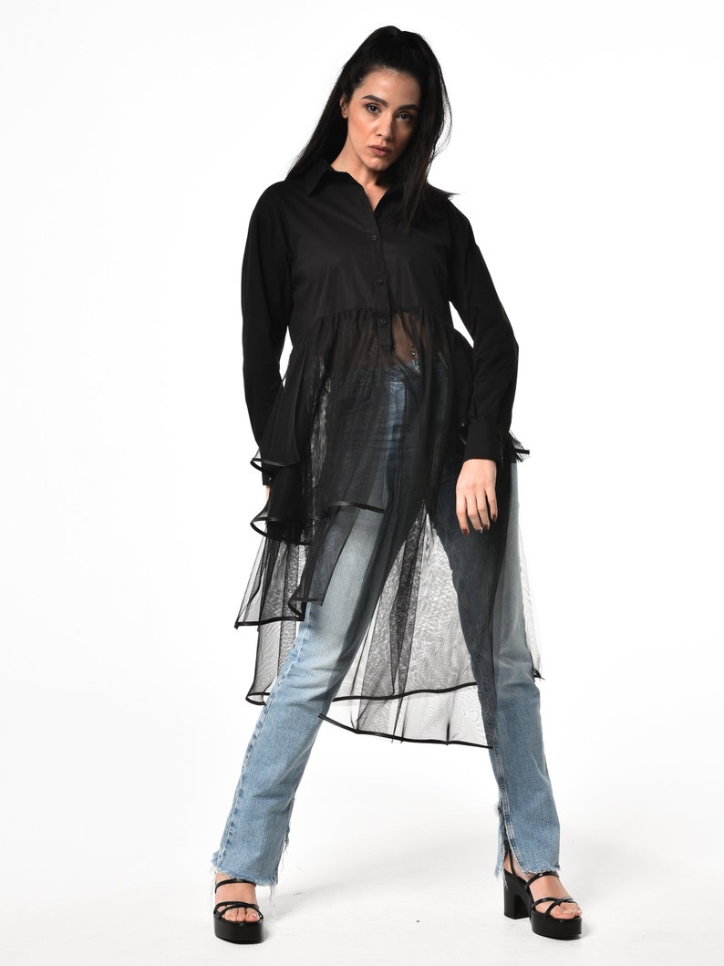 May include: A black long-sleeved shirt with a sheer overlay and a ruffled hem. The shirt is button-up and has a relaxed fit.