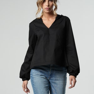 Puede incluir: Una blusa negra de manga larga con cuello en V y un detalle fruncido en las mu&ntilde;ecas. La blusa se lleva con pantalones vaqueros azules.