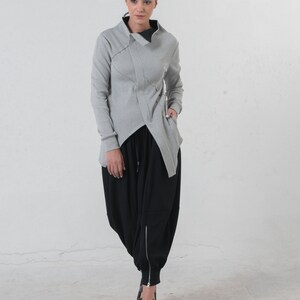 May include: A gray, asymmetrical, long-sleeved jacket with a high collar and a black, loose-fitting, drawstring pant.