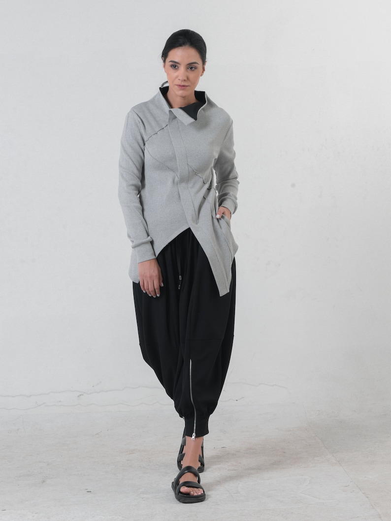 May include: A gray, asymmetrical, long-sleeved jacket with a high collar and a black, loose-fitting, drawstring pant.
