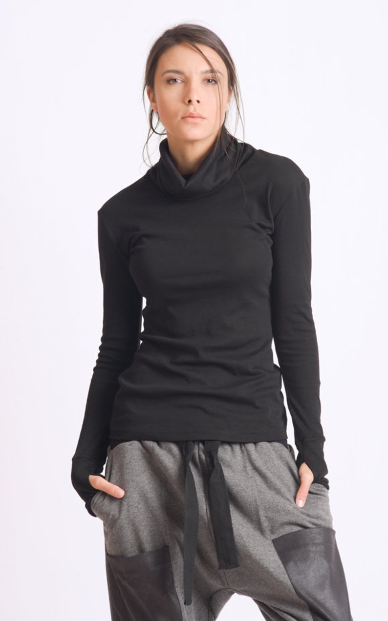 May include: A black long-sleeved shirt with a mock neck and thumbholes. The shirt is paired with gray pants with a black drawstring and black leather accents.
