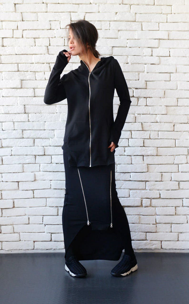 May include: A black hooded sweatshirt with a zipper and a matching black skirt with zipper details. The model is wearing black sneakers.