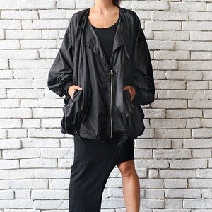 May include: A black oversized jacket with a zipper closure and a drawstring hood. The jacket has two pockets and is worn with a black skirt and black sneakers.