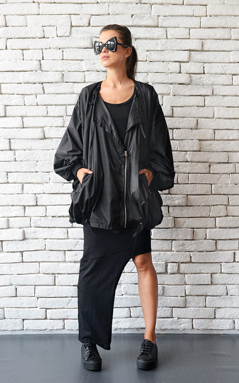 May include: A black oversized jacket with a zipper closure and a drawstring hood. The jacket has two pockets and is worn with a black skirt and black sneakers.