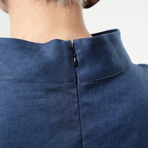 May include: A close-up of the back of a navy blue linen dress with a zip closure.