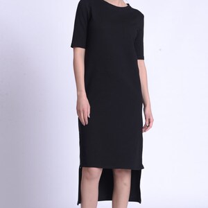 Puede incluir: Un vestido midi negro con un dobladillo alto-bajo. El vestido tiene un escote redondo y mangas cortas.