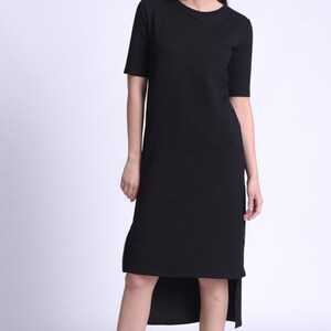Puede incluir: Un vestido negro de manga corta y corte asim&eacute;trico con cuello redondo. El vestido est&aacute; hecho de una tela suave y c&oacute;moda y tiene un corte holgado. La modelo lleva zapatillas negras.