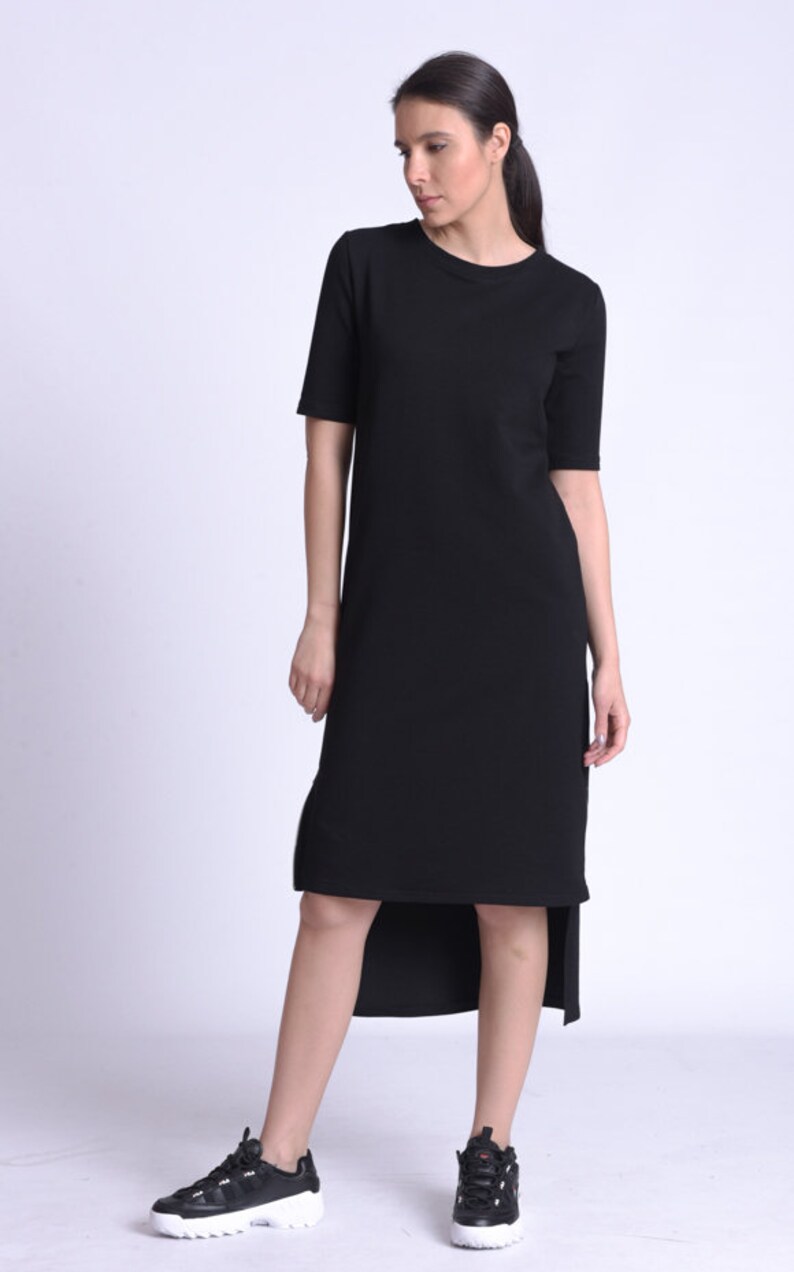 Puede incluir: Un vestido negro de manga corta y corte asim&eacute;trico con cuello redondo. El vestido est&aacute; hecho de una tela suave y c&oacute;moda y tiene un corte holgado. La modelo lleva zapatillas negras.