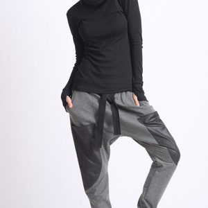 May include: A woman wearing a black mock neck shirt and gray sweatpants with black accents. The sweatpants have a drawstring waist and a loose fit.