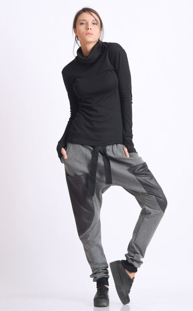 May include: A woman wearing a black mock neck shirt and gray sweatpants with black accents. The sweatpants have a drawstring waist and a loose fit.