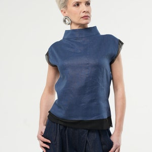 May include: A blue linen top with a mock neck and short sleeves. The sleeves have a black mesh trim. The top is layered over a black mesh tank top. The model is wearing blue denim trousers.