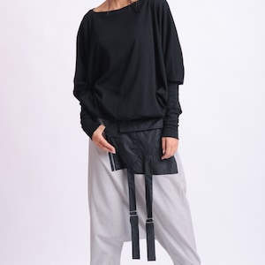 May include: A black long-sleeved top with a wide neckline and loose fit, paired with light gray, loose-fitting pants. The outfit includes a black waist pack with straps and black sneakers. The overall style is modern and minimalist.