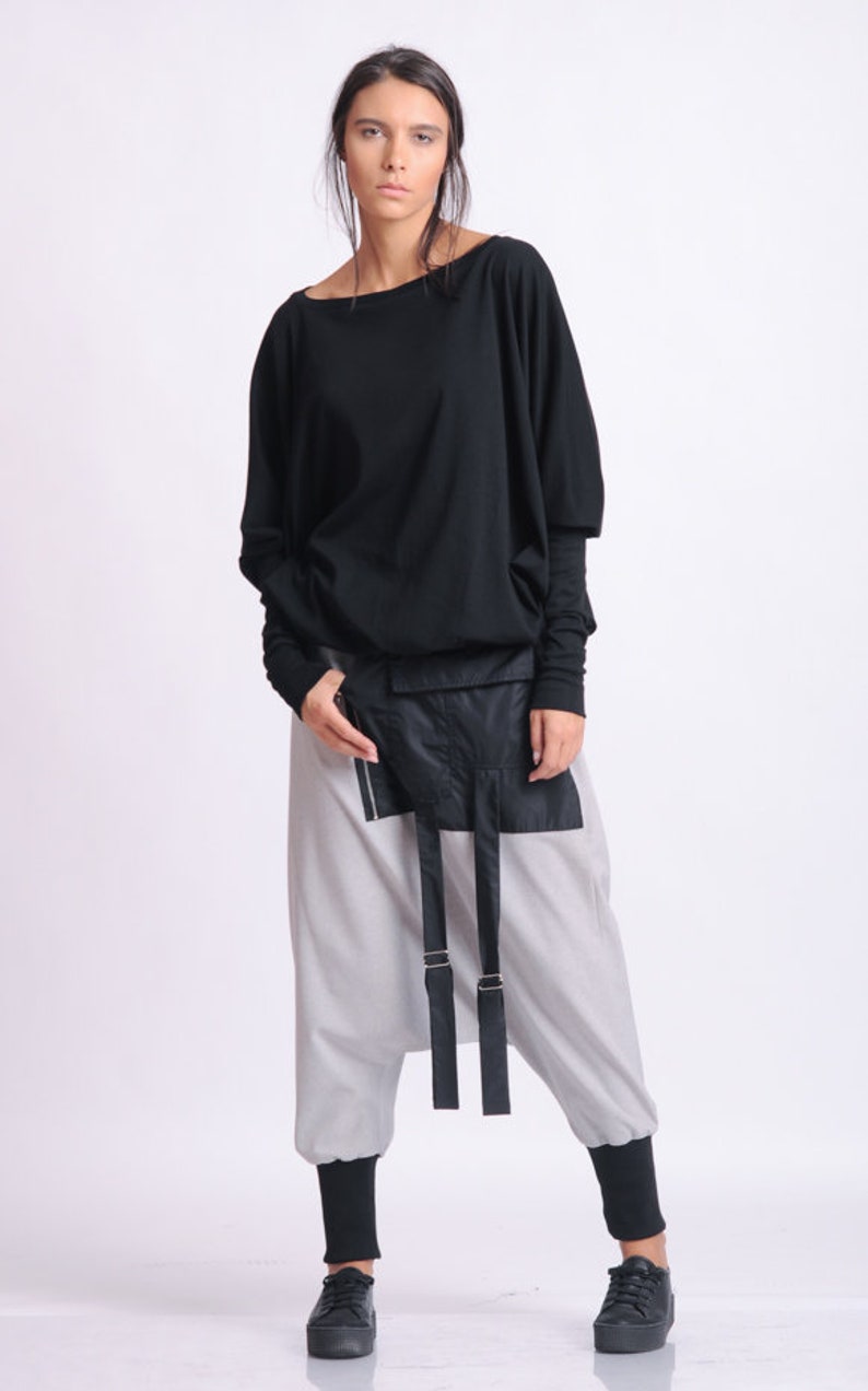 May include: A black long-sleeved top with a wide neckline and loose fit, paired with light gray, loose-fitting pants. The outfit includes a black waist pack with straps and black sneakers. The overall style is modern and minimalist.