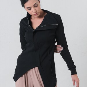 May include: A black long-sleeved shirt with a zippered collar and a long, asymmetrical hemline. The shirt is made of a ribbed fabric and has a relaxed fit.