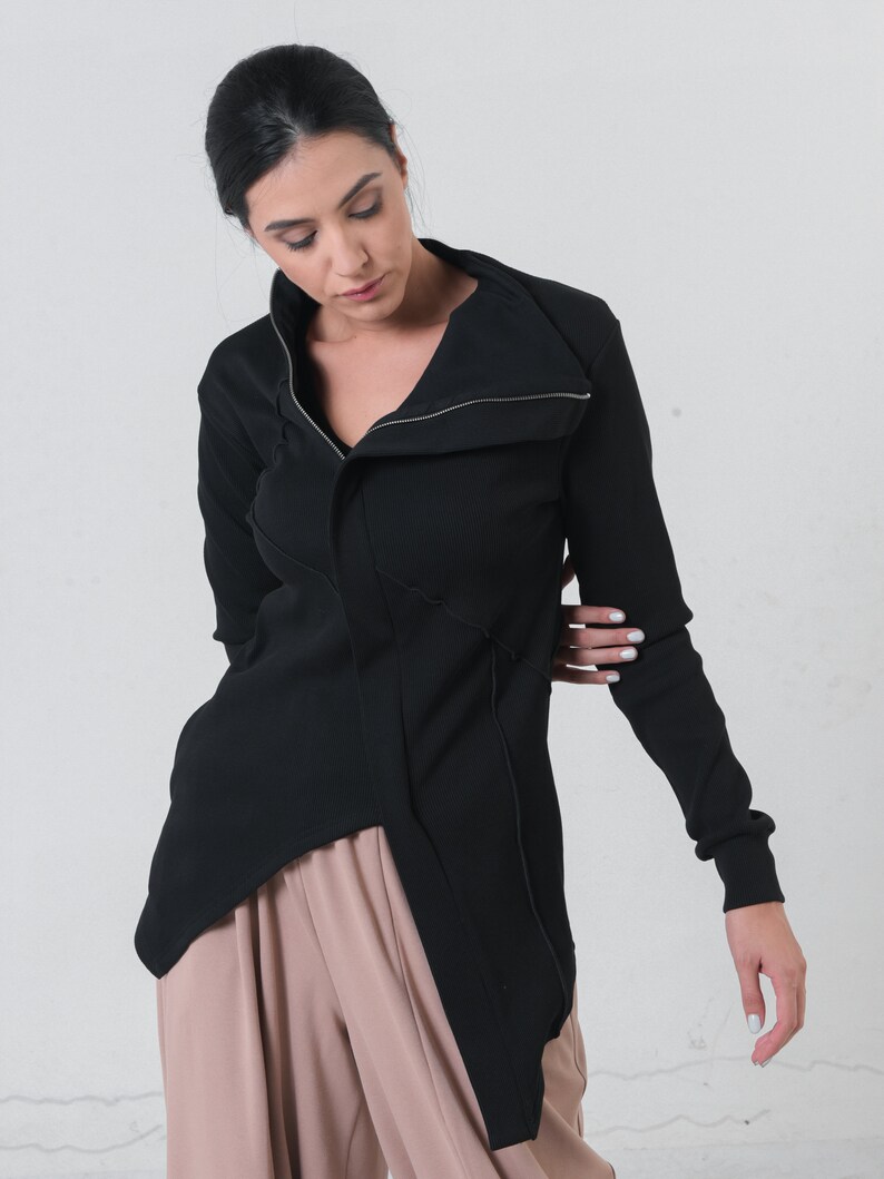 May include: A black long-sleeved shirt with a zippered collar and a long, asymmetrical hemline. The shirt is made of a ribbed fabric and has a relaxed fit.