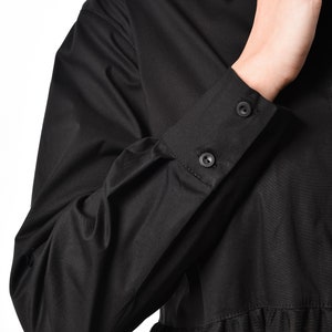 May include: Black long-sleeved shirt with a black tulle overlay. The shirt has a button-up collar and button cuffs.