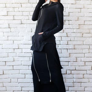 May include: A black hooded sweatshirt with a zipper and a black maxi skirt with multiple zippers. The skirt has a slight A-line shape and the sweatshirt has a long, flowing design.