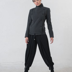 May include: A charcoal gray jacket with a high collar and double-breasted button closure. The jacket is paired with black, loose-fitting pants and black ankle boots. The outfit has a modern, minimalist aesthetic.