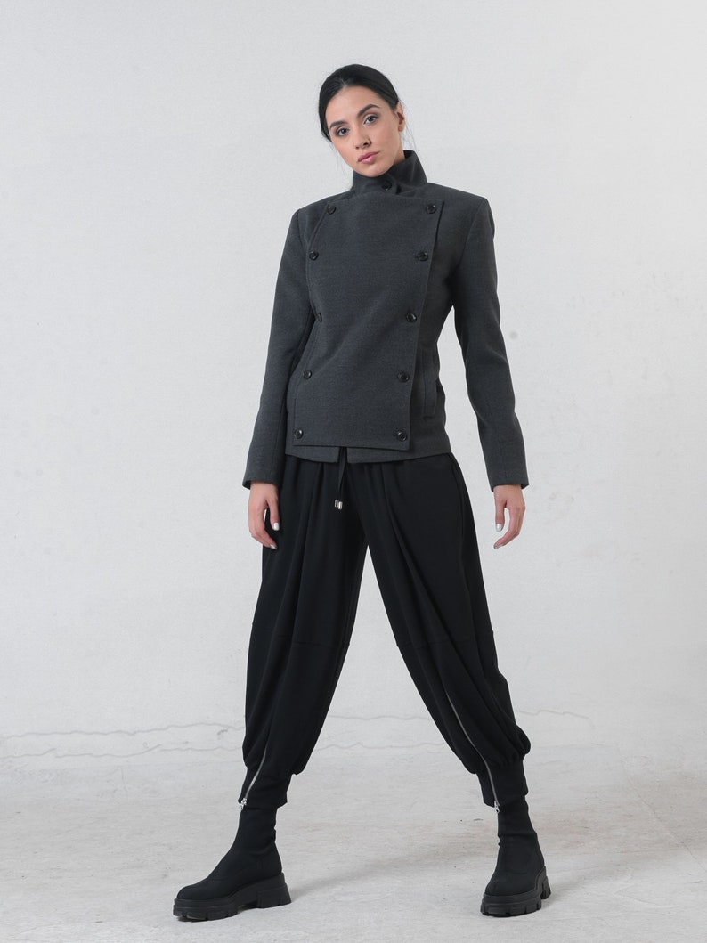May include: A charcoal gray jacket with a high collar and double-breasted button closure. The jacket is paired with black, loose-fitting pants and black ankle boots. The outfit has a modern, minimalist aesthetic.