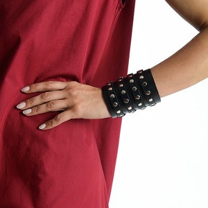 May include: A black leather cuff bracelet with silver studs. The bracelet is layered and has a punk rock aesthetic.