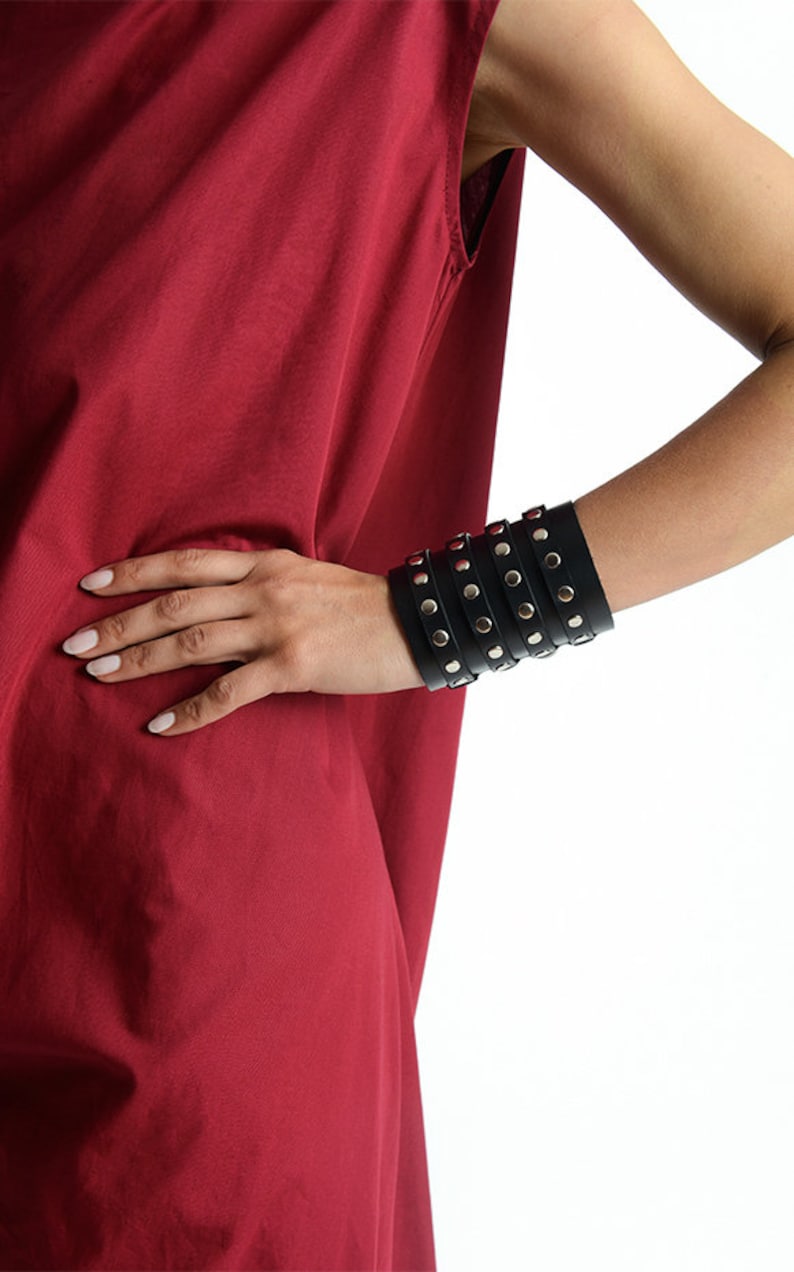 May include: A black leather cuff bracelet with silver studs. The bracelet is layered and has a punk rock aesthetic.