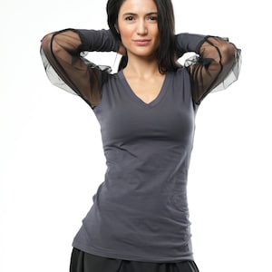 May include: A gray long-sleeved shirt with a V-neck and sheer black mesh sleeves. The shirt is fitted and has a casual style.