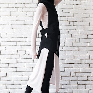 May include: A black long vest with a zipper and a high collar, worn over a pink long-sleeved shirt and black leggings. The person is wearing black high-top sneakers and black sunglasses.