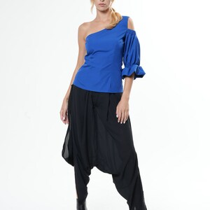May include: A woman wearing a royal blue one-shoulder top with a puffed sleeve and black harem pants.