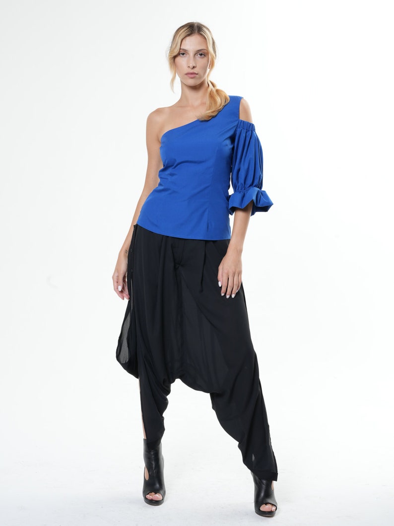 May include: A woman wearing a royal blue one-shoulder top with a puffed sleeve and black harem pants.
