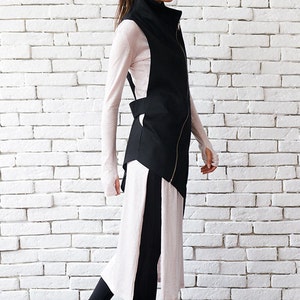 May include: A black asymmetrical vest with a zipper closure and a long, flowing pink and black skirt. The person is wearing black leggings and black high-top sneakers.