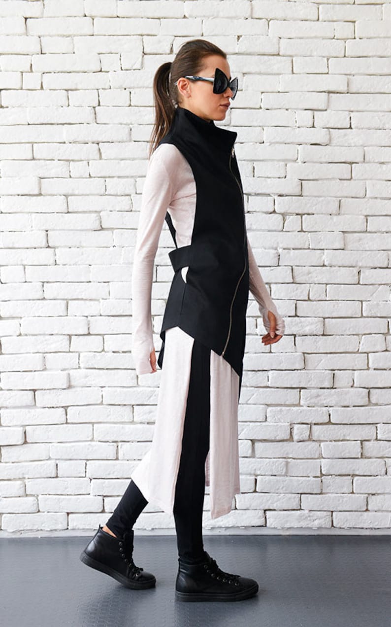 May include: A black asymmetrical vest with a zipper closure and a long, flowing pink and black skirt. The person is wearing black leggings and black high-top sneakers.