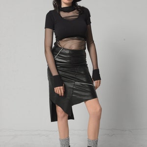 May include: A woman wearing a black mesh top, a black leather skirt with white stitching, black socks, and black platform boots. She is also wearing a black fedora.