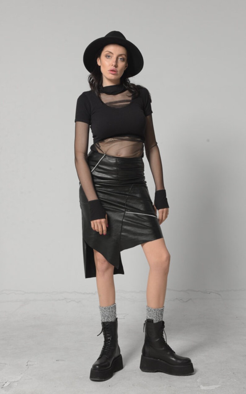 May include: A woman wearing a black mesh top, a black leather skirt with white stitching, black socks, and black platform boots. She is also wearing a black fedora.