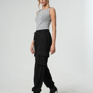 May include: A woman wearing a gray tank top and black cargo pants with a drawstring waist. She is wearing black heeled sandals.