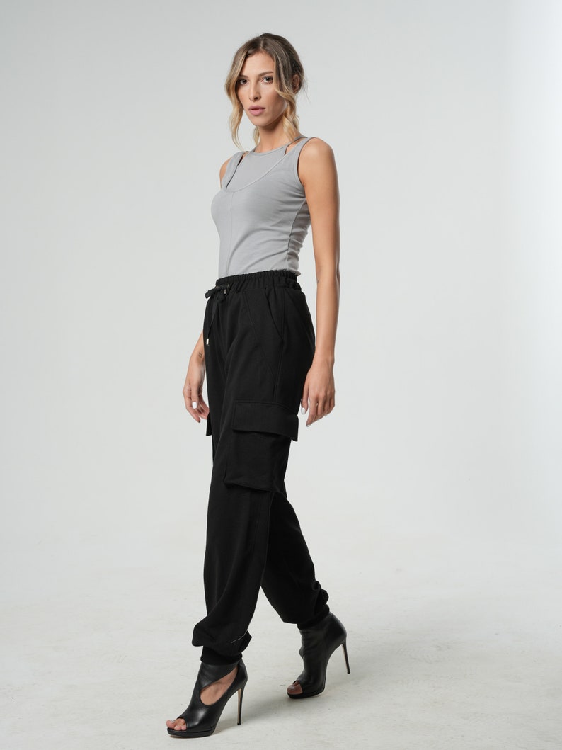 May include: A woman wearing a gray tank top and black cargo pants with a drawstring waist. She is wearing black heeled sandals.