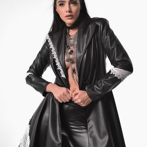 May include: A black leather jacket with white lace trim. The jacket is open and the person is wearing a silver chain necklace.
