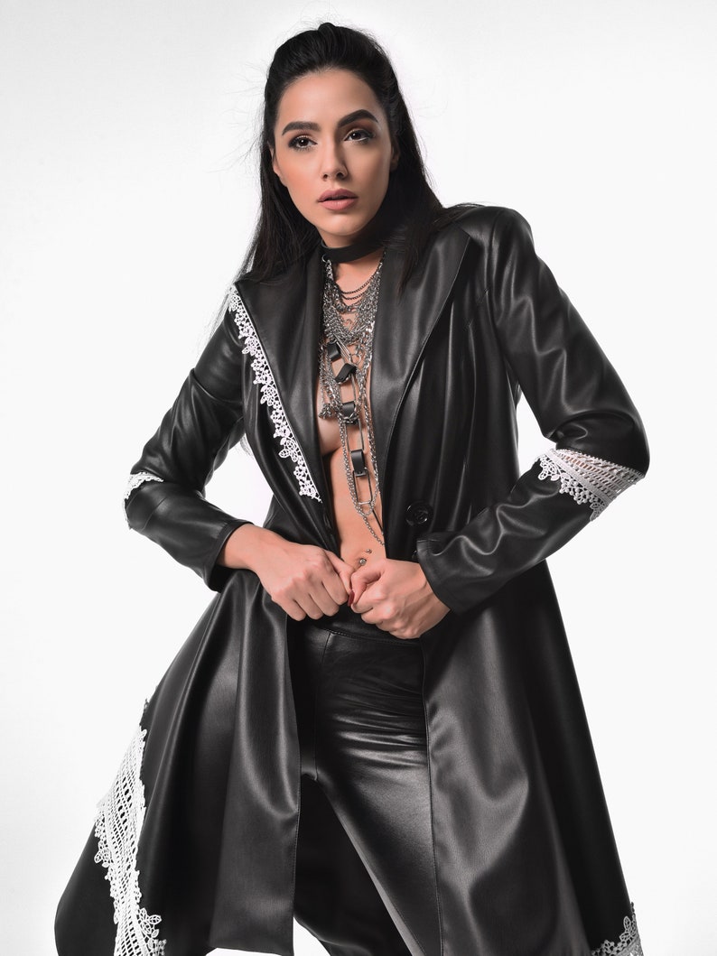 May include: A black leather jacket with white lace trim. The jacket is open and the person is wearing a silver chain necklace.