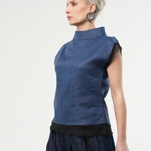 May include: A blue linen top with a mock neck and short sleeves. The sleeves have a black mesh trim. The top is paired with a dark blue denim skirt.