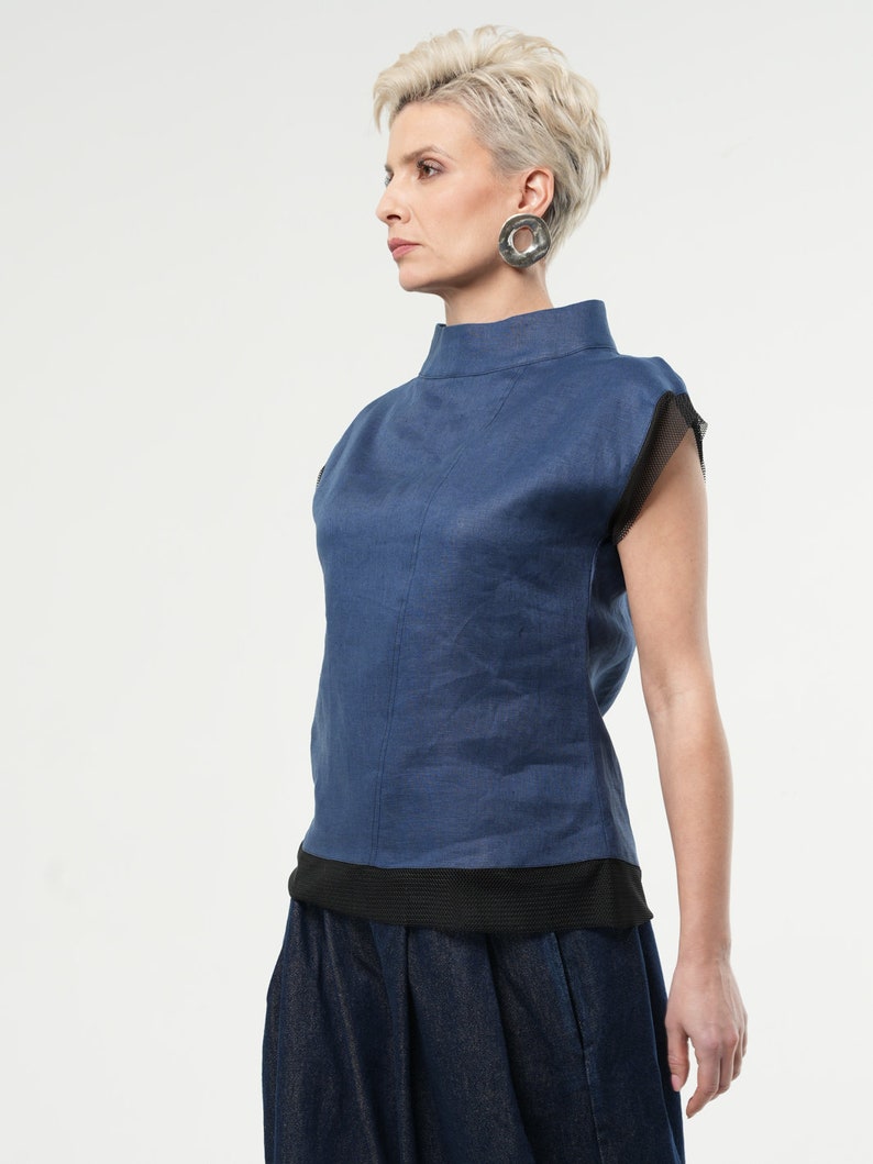 May include: A blue linen top with a mock neck and short sleeves. The sleeves have a black mesh trim. The top is paired with a dark blue denim skirt.