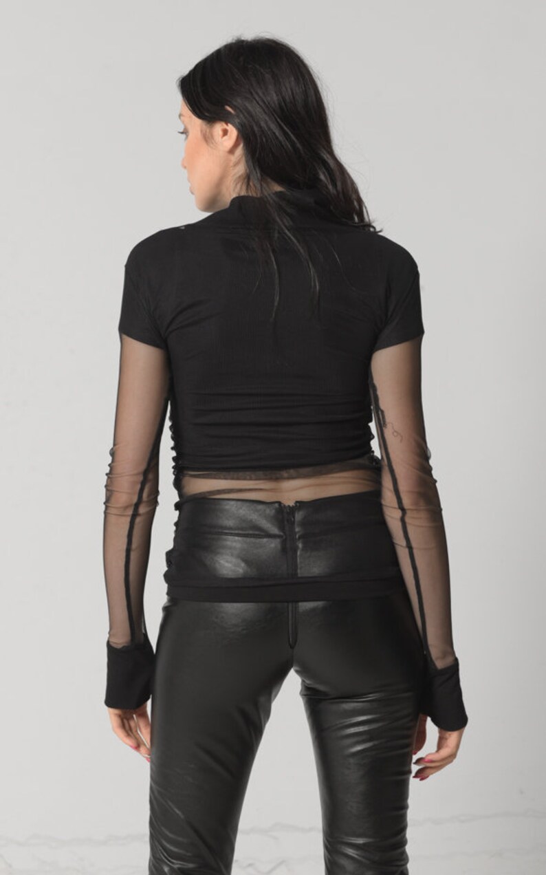 May include: Black long-sleeved shirt with a mesh overlay. The shirt has a fitted silhouette and a mock neck.