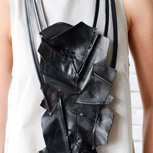 May include: A black leather necklace with a geometric design. The necklace is made of multiple pieces of leather that are stitched together to create a unique and modern look.