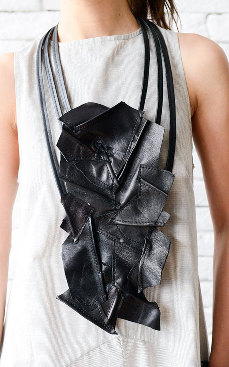May include: A black leather necklace with a geometric design. The necklace is made of multiple pieces of leather that are stitched together to create a unique and modern look.