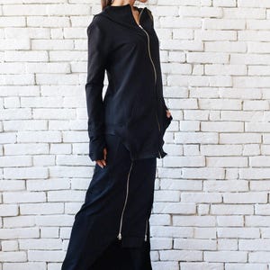 May include: A black long-sleeved jacket with a zipper and a black skirt with a zipper detail. The person is wearing black sneakers.