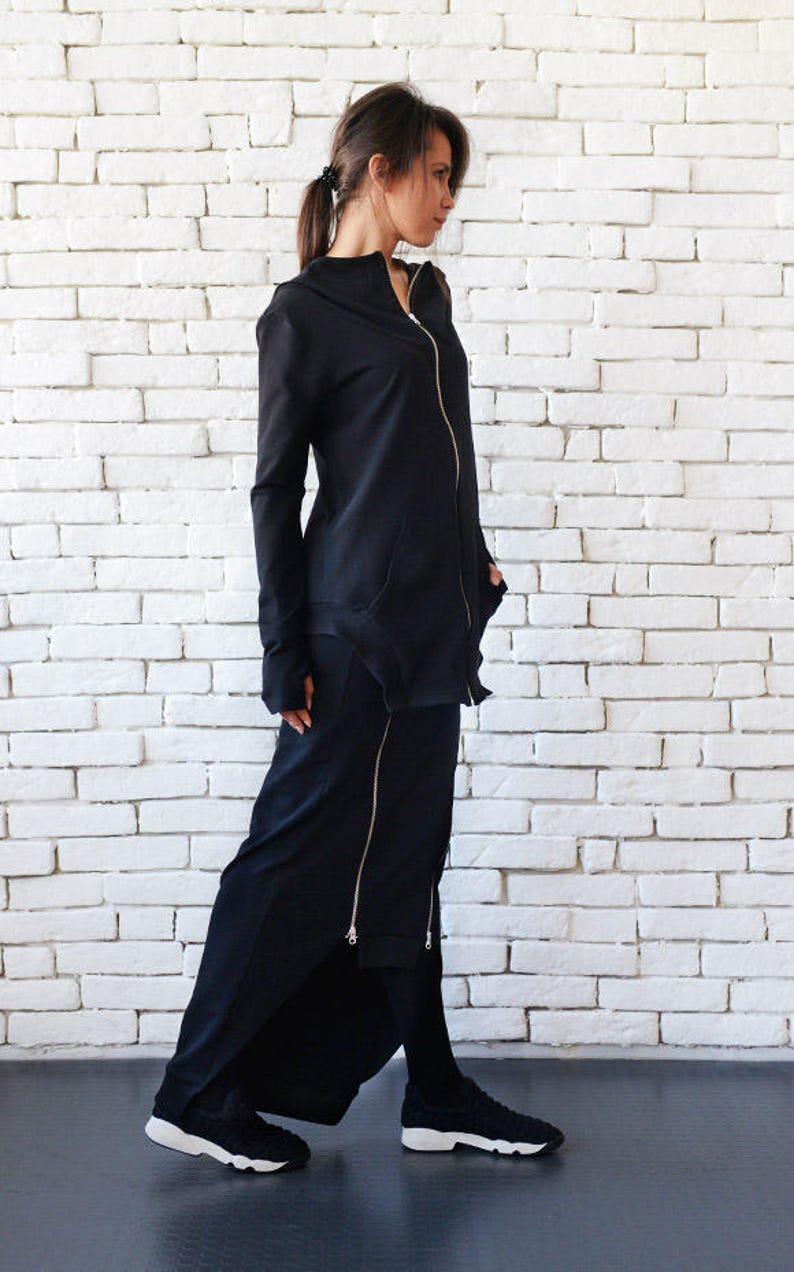 May include: A black long-sleeved jacket with a zipper and a black skirt with a zipper detail. The person is wearing black sneakers.